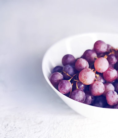Purple grapes in a simple white bowl, presenting a fresh, healthy, and organic fruit choice for a balanced dietの写真素材