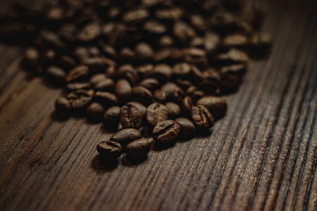Roasted coffee beans creating a textured pattern on a dark wood surface, emphasizing freshness and coffee cultureの写真素材
