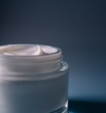 Creamy white cosmetic product in a clear glass jar with a textured peak, highlighting beauty,...