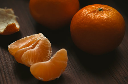 Peeled tangerine segments with whole mandarin oranges and discarded skin on a dark wooden table, highlighting healthy eatingの写真素材