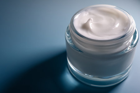 White cosmetic cream in an open glass jar, representing skincare, beauty, and well being on a blue backgroundの写真素材