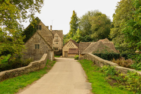 The picturesque village of Stourhead boasts a charming road that crosses a historic stone bridge, nestled amidst verdant greenery and quaint English cottagesの写真素材