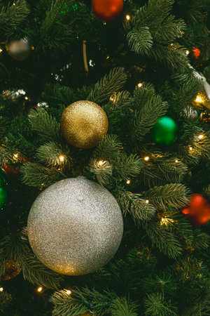 Christmas tree branches holding colorful, shimmering ornaments and glowing string lights, creating a festive holiday decoration backgroundの写真素材