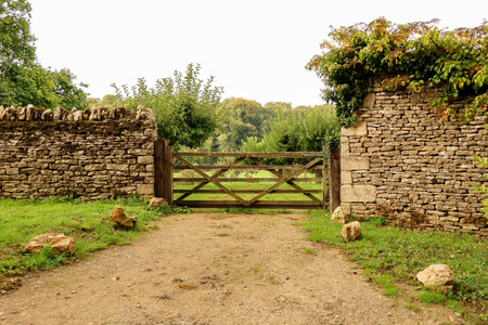 Rustic wooden gate protecting an entrance to a countryside field. Dry stone walls line the path, surrounded by lush green foliageの写真素材