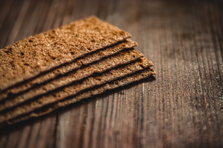 Stacked rectangular rye crispbread crackers resting on a textured dark wood surface, emphasizing...