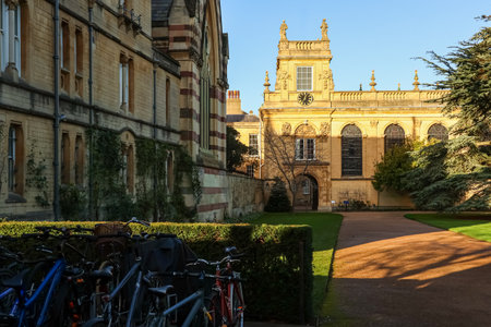 Ancient university grounds displaying classic English architecture, a green lawn, and numerous bicycles parked on a sunny dayの写真素材