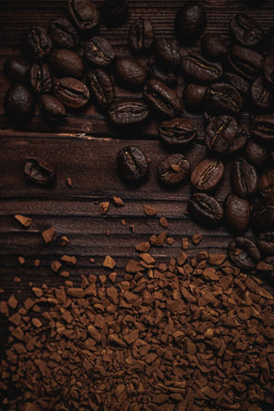 Roasted coffee beans and instant coffee granules scattered on a dark wooden surface, illustrating...
