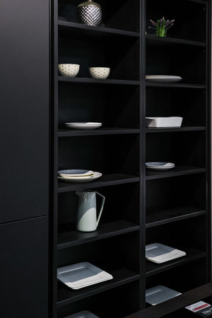 Modern minimalist cabinet featuring black open shelves with various kitchen ceramics, plates, bowls, a jug, and decorative elementsの写真素材