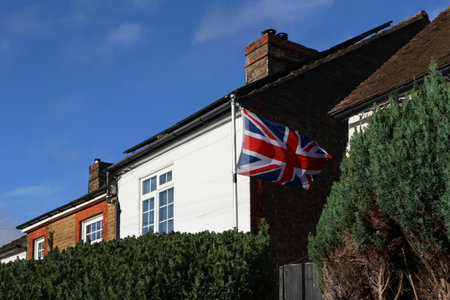 Union Jack flag flying proudly from a residential house, symbolizing patriotism and independence in the United Kingdomの写真素材