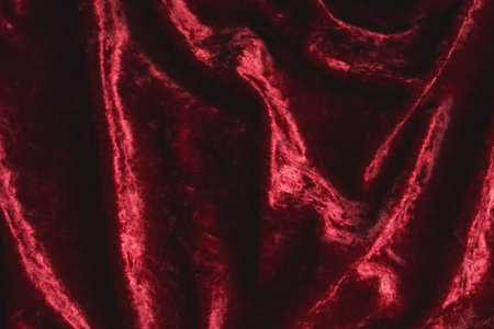 Deep red velvet fabric showing soft folds and a textured surface, evoking luxury and elegance with draping materialの写真素材