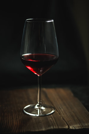 Red wine pouring into a crystal glass, sitting elegantly on a dark wooden surface. Romantic mood, ideal for celebrationsの写真素材