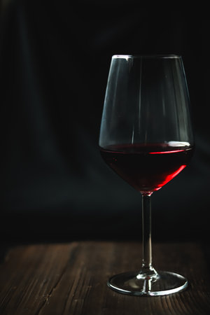 Glass of dark red wine on a rustic wooden surface with a soft, moody light, highlighting liquid, drink, alcoholの写真素材