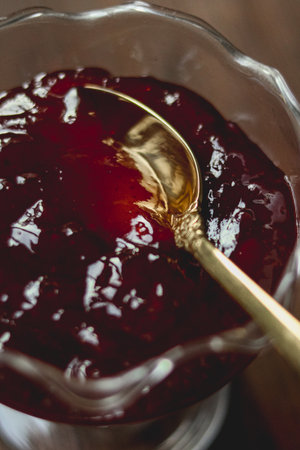 Red berry jam in a glass dish, an elegant golden spoon resting in the sweet fruit spread. Preparing homemade dessertの写真素材