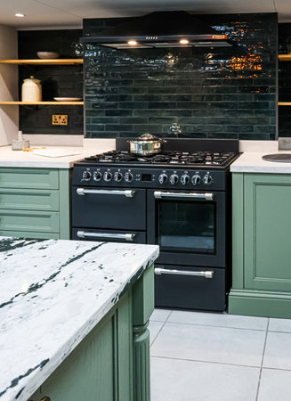 Modern kitchen with sage green cabinets, a large black cooker range, and shiny subway tile...