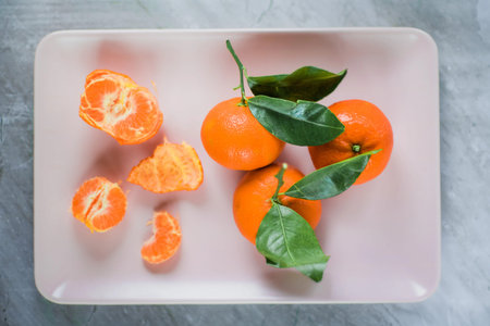 Fresh tangerines rest beside green leaves on a pink rectangular tray, their peeled segments highlighting vitaminc benefits for a healthy lifestyle