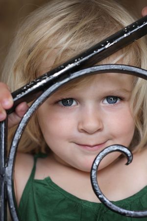 A 3 year old girl peeping through a wrought iron fence with a sweet smile. Happy, positive feelingの写真素材