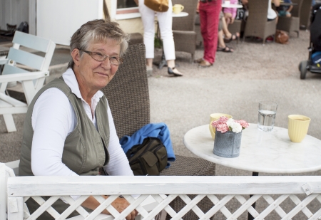 Happy retired pensioner woman sitting alone in an outdoor cafeの写真素材