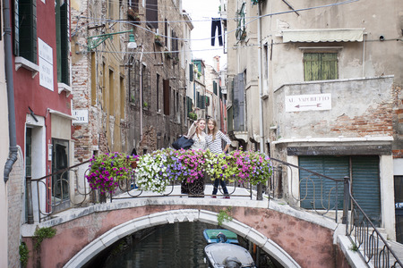Two young women on a bridge over a canal in Venice, Italyの写真素材
