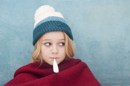 Close up of child with fever thermometer, wrapped in blanket, Space for textの写真素材