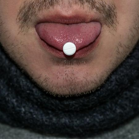 Round white tablet on the tongue. Detail of the face of a man with a mustache and beard.の写真素材
