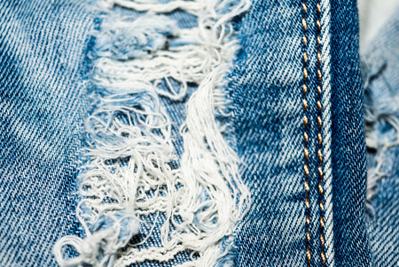 Holey jeans. Blue denim texture. Threads, seam. Close-up.