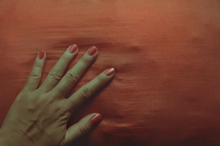 Retro Manicured Hand with Orange Nail Polish Fanning on Orange Cushionの写真素材