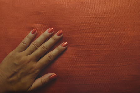Manicured Female Hand with Orange Nail Polish on Orange Pillow - Matching Colorsの写真素材