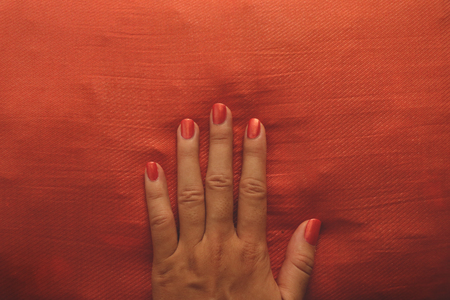 Manicured Hand with Orange Nail Polish on Matching Pillowの写真素材