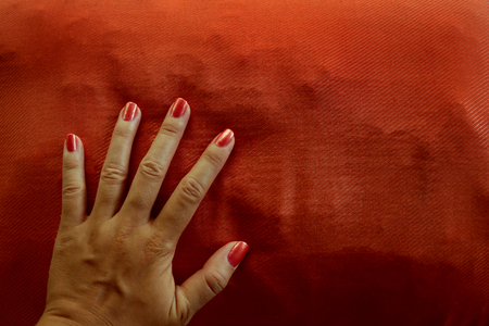 Manicured Female Hand with Bright Orange Nail Polish on Matching Cushionの写真素材