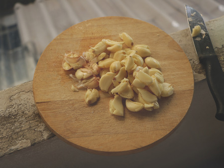 Freshly Peeled and Smashed Garlic on Wooden Cutting Board with Knife - Dirty Apartment Balconyの写真素材