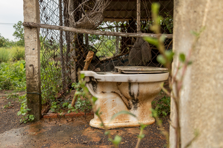 Abandoned Vintage Old Toilet on Wet Concrete Ground - Green Countryside Garden/ Wire Fence/ Water PVC Pipes - Side Viewの写真素材