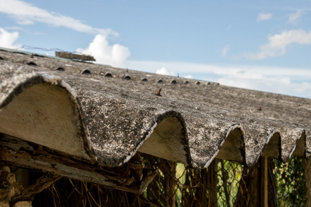 Dirty Moldy Corrugated Roof of Abandoned Asian Chicken Coop with Rusty Wire Fence - Blue Bright Sky with Cloudsの写真素材
