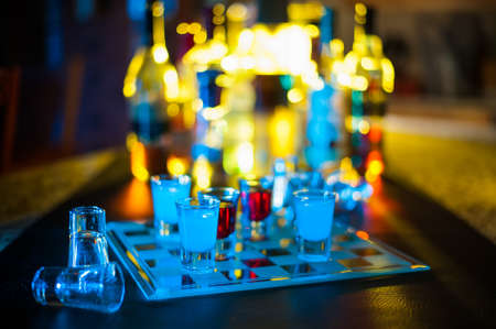 A bar game of shot glass checkers with back lit bottles behind the scene.の写真素材