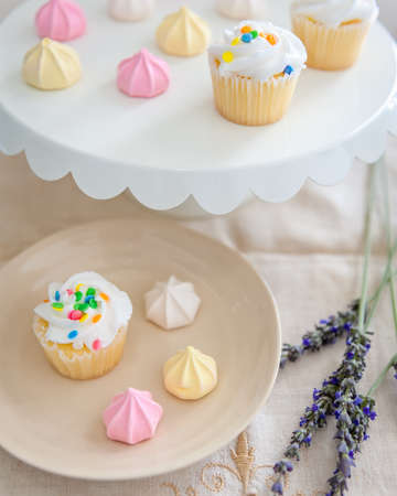 A cake plate and dessert plate filled with confetti sprinkled cupcakes and pastel colored meringue bite cookies.の写真素材