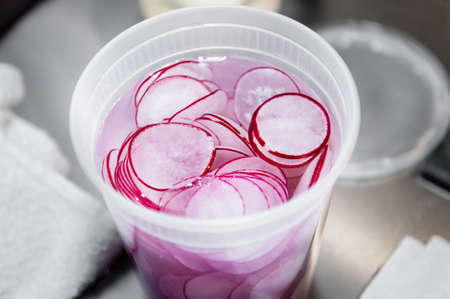 Freshly sliced radishes are prepped for dinner and stored in a white container with water in order to keep them crispy.の写真素材