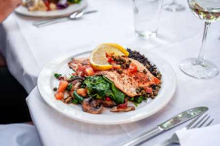 A plate of freshly served ruby red trout with rice and assorted vegetables placed on a white tablecloth.の写真素材