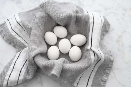 Hardboiled eggs in a container lined with a gray and white striped towel sitting on a white marble countertop.の写真素材