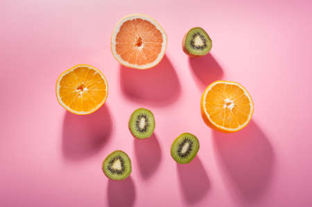 Fruits with high levels of Vitamin C-- kiwi, orange and grapefruit--in direct lighting on a pink background.の写真素材