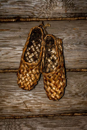 Ancient Russian shoes - woven bast shoes close-up hang on a nail against the background of a log...