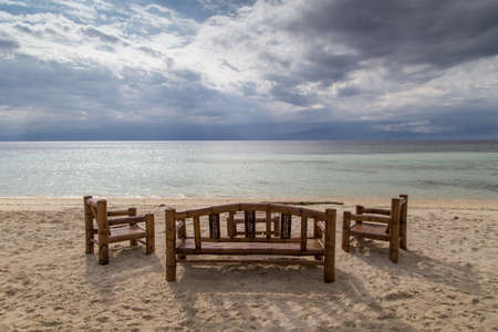 A table with brown chairs. On the shore of a sandy beach overlooking the sea and clouds. On the Sunset.の写真素材