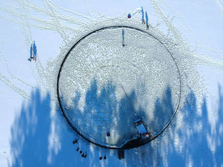 A large hole was cut out on a frozen lake. They made a big roundabout out of it, attaching the motor from the boat made it move. Shot from the sky, view from above. Horizontal orientationの写真素材