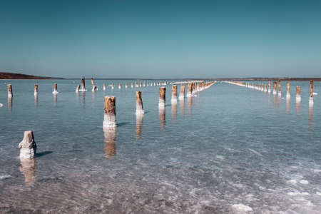 Salt lake in the south of Ukraine with mud baths. Treatment in a salt lake. Sanatorium. Blue sky on a sunny day. Wooden posts for salt miningの写真素材
