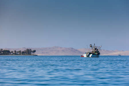A fishing boat stands on the sea near the shore with palm trees and a view of the desertの写真素材