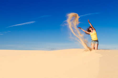 Woman in a yellow top in the desert against the blue sky, throws sandの写真素材