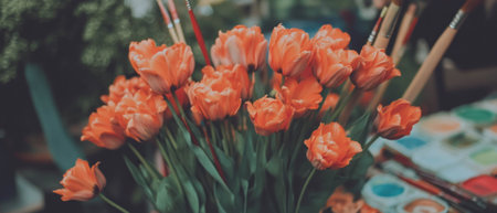 Vibrant orange tulips and paintbrushes in a creative artistic settingの素材
