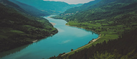 Cinematic view of a tranquil river winding through a lush green valley landscapeの写真素材