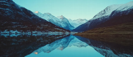 Majestic snow-covered mountains reflecting in a tranquil fjord at dawnの素材
