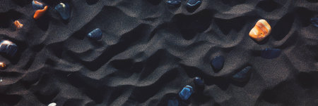 Textured black sand with pebbles glistening in deep shadowsの素材