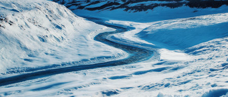 Winding frozen river through a snowy valley creating a serene winter landscapeの写真素材