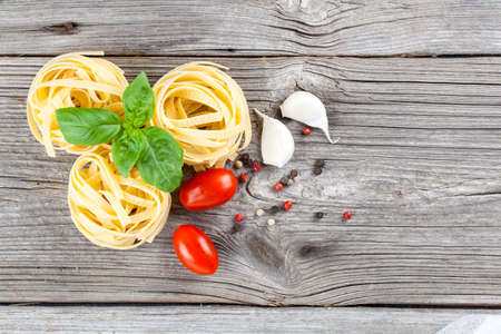 Italian pasta fettuccine nest with garlic, tomatoes and fresh basil leaves, on wooden backgroundの写真素材